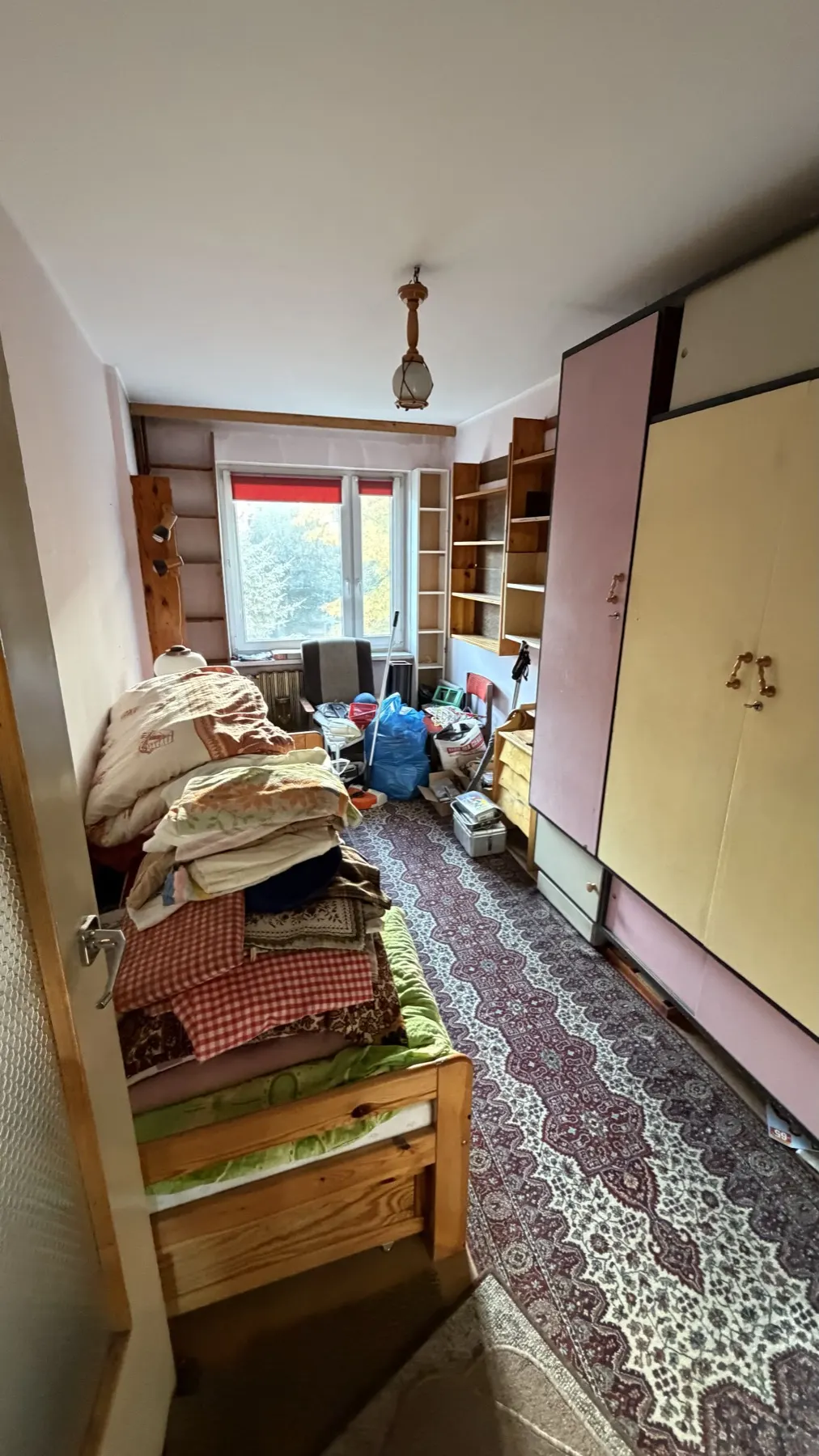 Drugi pokój w Tychach przed opróżnieniem: łóżko, szafa i rzeczy na podłodze